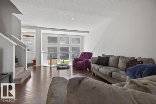 Spacious living area featuring rich wood-finish flooring, a contemporary window wall, white trim, light gray wall paint, and a textured ceiling - 17540 58 Street Nw, Edmonton, AB 