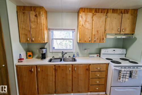 Kitchen featuring natural wood cabinetry, light countertops, a stainless steel double basin sink, and a four-burner electric range - 331 60417 Range Road 124, Rural St. Paul County, AB 