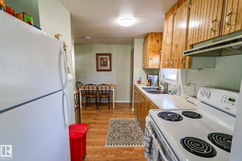 Kitchen featuring wood-finish flooring, wood cabinetry with decorative hardware, white countertop, white stove with overhead ventilation, and a stainless steel sink - 331 60417 Range Road 124, Rural St. Paul County, AB 