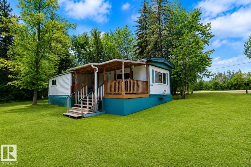 White siding residence featuring a covered wooden porch with railings, set on a bright green lawn - 331 60417 Range Road 124, Rural St. Paul County, AB 