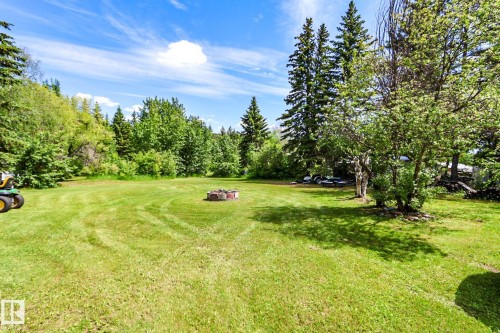 Expansive green lawn with a built-in fire pit, surrounded by mature trees and natural foliage - 331 60417 Range Road 124, Rural St. Paul County, AB 