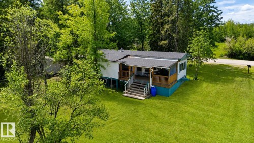 Single-story residence featuring a covered front porch with wood railings and steps, set on a bright green lawn - 331 60417 Range Road 124, Rural St. Paul County, AB 