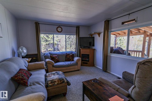 Carpeted living area featuring paneling and beadboard wall finishes, a built-in corner entertainment cabinet with an electric fireplace, and multiple windows providing natural light - 331 60417 Range Road 124, Rural St. Paul County, AB 