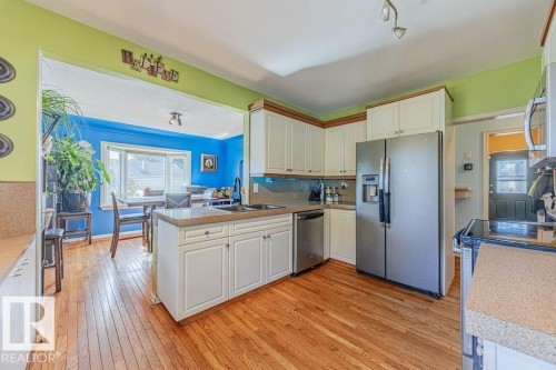 Kitchen featuring wood-finish flooring, light cabinetry, and stainless-steel appliances - 12339 89 Street, Edmonton, AB - Indoor Photo Showing Kitchen