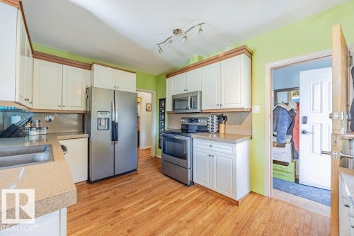 Kitchen featuring wood-finish flooring, light cabinetry, and stainless-steel appliances - 12339 89 Street, Edmonton, AB - Indoor Photo Showing Kitchen