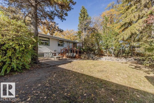 Rear exterior featuring white horizontal siding, a wooden deck, and a stone-lined dry creek bed with a decorative wooden bridge - 12339 89 Street, Edmonton, AB - Outdoor