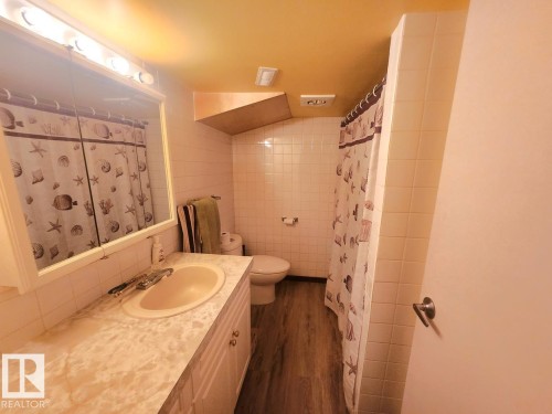 Bathroom featuring a single-sink vanity with patterned countertop, white cabinetry, and wood-finish flooring - 12339 89 Street, Edmonton, AB - Indoor Photo Showing Bathroom