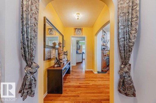 Hardwood flooring throughout a living space featuring a fireplace with a decorative mantel and an arched entryway - 12339 89 Street, Edmonton, AB - Indoor Photo Showing Living Room With Fireplace