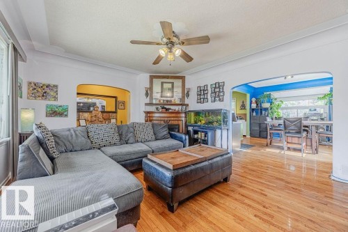 Spacious living area featuring expansive windows, wood-finish flooring, a ceiling fan with integrated lighting, and a built-in media console with shelving - 12339 89 Street, Edmonton, AB - Indoor Photo Showing Living Room