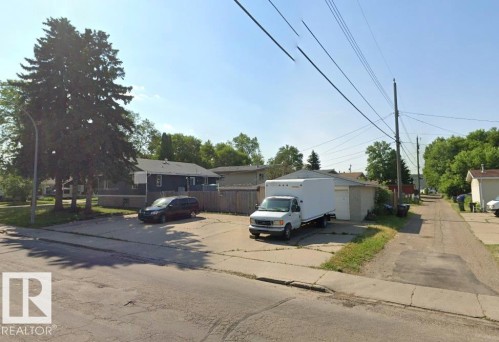 Paved lot featuring a detached garage with a roll-up door, partial fencing, and mature trees - 11834 44 Street, Edmonton, AB - Outdoor