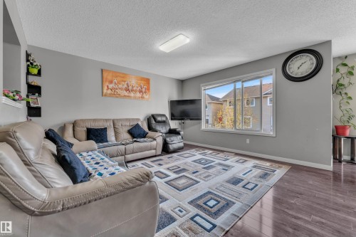 Spacious living area featuring wood-finish flooring, a large window, light gray walls, and a flat ceiling with a flush-mount light fixture - 5520 5 Avenue, Edmonton, AB - Indoor Photo Showing Living Room