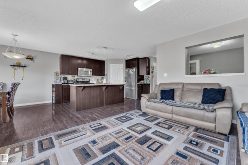 Open-concept living space featuring wood-finish flooring, a kitchen island with seating, dark wood cabinetry, and stainless steel appliances - 5520 5 Avenue, Edmonton, AB - Indoor Photo Showing Kitchen