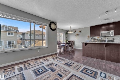 Expansive window framing exterior houses, wood-finish flooring, dark cabinetry, stainless steel appliances, and track lighting - 5520 5 Avenue, Edmonton, AB - Indoor Photo Showing Kitchen
