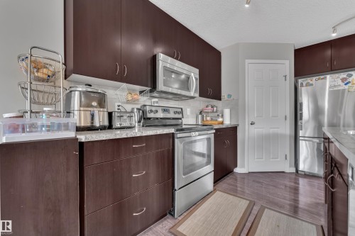 Kitchen featuring dark wood-finish cabinetry, stainless steel appliances, light-toned countertops, a white subway tile backsplash, and wood-finish flooring - 5520 5 Avenue, Edmonton, AB - Indoor Photo Showing Kitchen