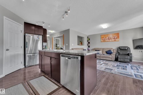 Kitchen island featuring a stainless steel dishwasher, brown cabinetry, and a light-toned countertop - 5520 5 Avenue, Edmonton, AB - Indoor Photo Showing Kitchen