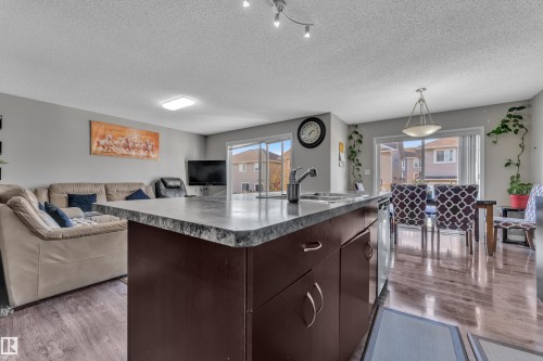 Kitchen island with dark wood-finish cabinetry, a stone-finish countertop, and an undermount sink - 5520 5 Avenue, Edmonton, AB - Indoor Photo Showing Other Room
