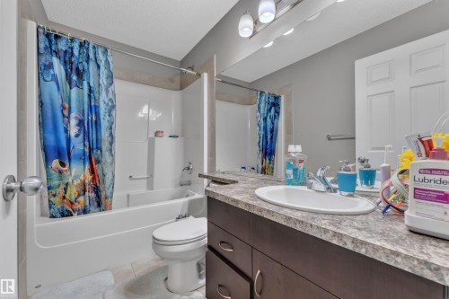 Bathroom featuring a full-size bathtub with integrated shower, single vanity with a laminate countertop, undermount sink, and a large wall-mounted mirror - 5520 5 Avenue, Edmonton, AB - Indoor Photo Showing Bathroom