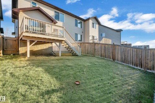 Expansive green space featuring a wood-plank deck with balusters and stairs, tan horizontal siding, multiple windows, and a wood privacy fence - 5520 5 Avenue, Edmonton, AB - Outdoor With Deck Patio Veranda