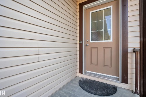 Front entry featuring a paneled door with grid-patterned window, dark brown trim, light beige siding, and a gray textured porch floor - 5520 5 Avenue, Edmonton, AB - Outdoor With Exterior