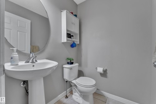 Pedestal sink with a chrome faucet, oval wall mirror, wall-mounted storage cabinet, and tiled flooring - 5520 5 Avenue, Edmonton, AB - Indoor Photo Showing Bathroom