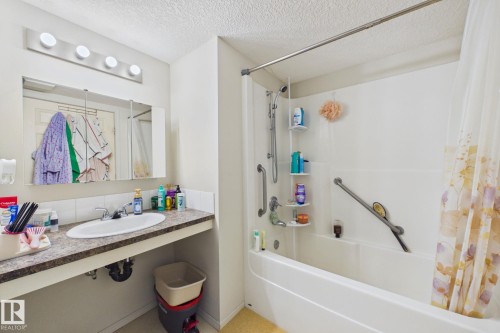 Bathroom featuring a white bathtub and shower combination with grab bars, a vanity with an integrated sink, a large mirrored medicine cabinet, and overhead four-bulb lighting - 220 80A Kelloway Crescent, Red Deer, AB - Indoor Photo Showing Bathroom