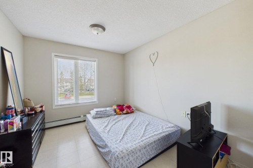 Neutral wall paint, textured ceiling, and a large window with blinds - 220 80A Kelloway Crescent, Red Deer, AB - Indoor Photo Showing Bedroom