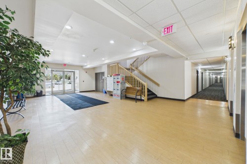 Spacious common area featuring light wood-finish flooring, a contemporary staircase with wood railings, multiple recessed lighting fixtures, and direct access to an elevator bank - 220 80A Kelloway Crescent, Red Deer, AB - Indoor Photo Showing Other Room