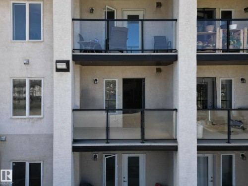Multi-story building facade featuring textured exterior finish and multiple private balconies with glass and black metal railings - 220 80A Kelloway Crescent, Red Deer, AB - Outdoor With Balcony