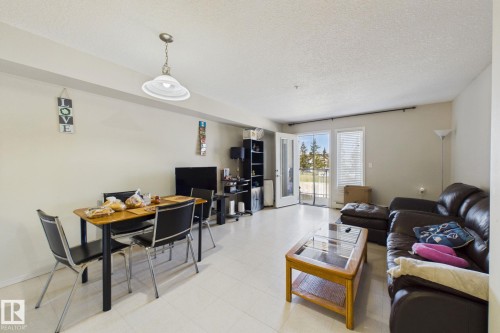 Spacious living area featuring light-toned flooring, white walls, and a glass-paneled double door leading to an outdoor balcony - 220 80A Kelloway Crescent, Red Deer, AB - Indoor Photo Showing Other Room