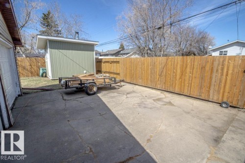 Concrete patio area featuring a detached storage shed with light green siding and a private wood fence - 4822 45 Ave, St. Paul Town, AB - Outdoor