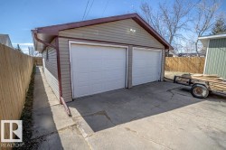 Detached two-car garage with overhead doors, light-toned siding, dark trim, and a concrete driveway - 