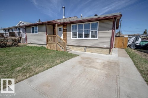 Light-colored siding exterior featuring a natural wood-finish accent wall, white-framed windows, and a concrete driveway - 4822 45 Ave, St. Paul Town, AB - Outdoor