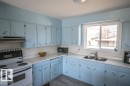 Kitchen featuring light blue cabinetry, white countertops, a white tile backsplash, and wood-finish flooring - 4822 45 Ave, St. Paul Town, AB  - Indoor Photo Showing Kitchen With Double Sink 