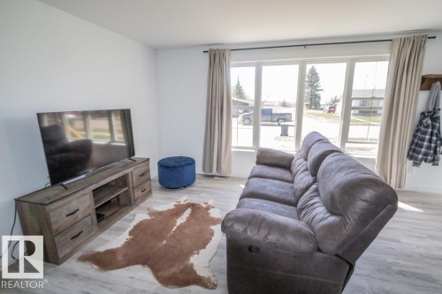 Living area featuring light wood-finish flooring, a wood-look media console with dark hardware, and a large window with white framing - 4822 45 Ave, St. Paul Town, AB - Indoor Photo Showing Living Room