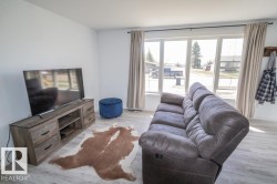 Living area featuring light wood-finish flooring, a wood-look media console with dark hardware, and a large window with white framing - 