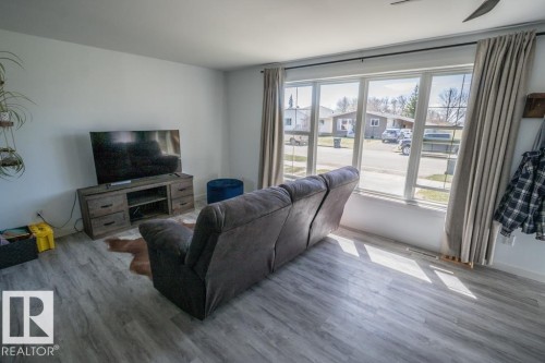 Spacious living area featuring light-tone wood-finish flooring and a multi-pane window with drapery rods - 4822 45 Ave, St. Paul Town, AB - Indoor Photo Showing Living Room