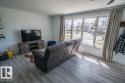 Spacious living area featuring light-tone wood-finish flooring and a multi-pane window with drapery rods - 
