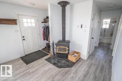 Entryway featuring wood-finish flooring, a black wood-burning stove with a tile hearth, and a white paneled door with glass inserts - 4822 45 Ave, St. Paul Town, AB - Indoor Photo Showing Other Room