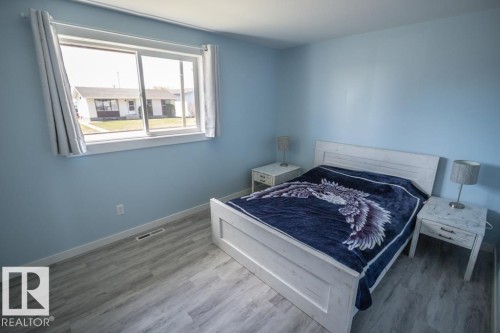 Bedroom featuring a large sliding window with white trim, light blue walls, and wood-finish flooring - 4822 45 Ave, St. Paul Town, AB - Indoor Photo Showing Bedroom