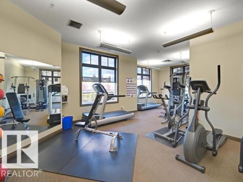 Dedicated fitness room featuring cardio and strength equipment, mirrored wall, large windows, recessed lighting, and carpet flooring with protective mats - 109 160 Magrath Rd, Edmonton, AB 