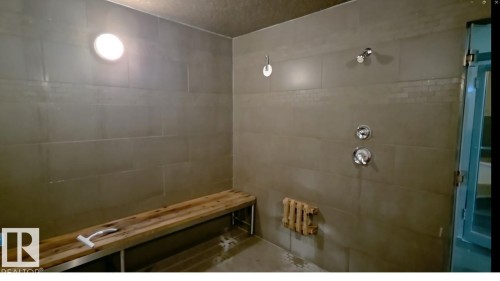 Spacious tiled shower with a built-in wooden bench, chrome fixtures, and integrated lighting - 109 160 Magrath Rd, Edmonton, AB 