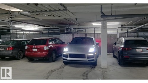 Underground parking garage featuring concrete flooring, exposed utility piping, and fluorescent lighting - 109 160 Magrath Rd, Edmonton, AB 