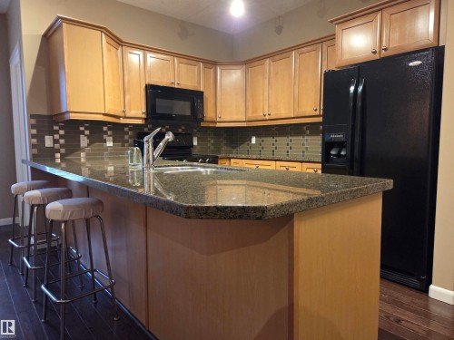Open-concept kitchen featuring an island with an undermount sink, granite countertops, and wood-finish cabinetry - 109 160 Magrath Rd, Edmonton, AB - Indoor Photo Showing Kitchen With Double Sink