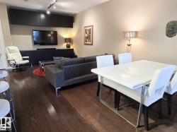 Spacious open-concept living area featuring rich wood-finish flooring, track lighting, and built-in dark cabinetry - 
