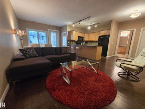 Open concept living space featuring dark wood-finish flooring, a kitchen with light wood cabinetry, a breakfast bar, and a tile backsplash - 109 160 Magrath Rd, Edmonton, AB - Indoor Photo Showing Living Room