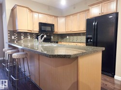 Kitchen featuring light wood cabinetry, dark granite countertops, and a mosaic tile backsplash - 