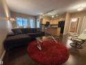 Open concept living space featuring dark wood-finish flooring, a kitchen with light wood cabinetry, a breakfast bar, and a tile backsplash - 109 160 Magrath Rd, Edmonton, AB  - Indoor Photo Showing Living Room 