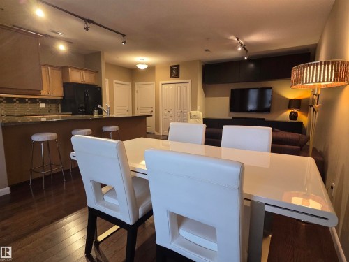 Kitchen and dining area featuring wood-finish flooring, a breakfast bar, stone countertops, and a tiled backsplash - 109 160 Magrath Rd, Edmonton, AB - Indoor