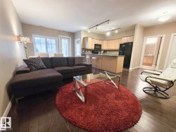 Open-concept living space featuring wood-finish flooring, a kitchen island with seating, natural wood cabinetry, and track lighting - 