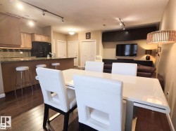 Open-concept living space featuring wood-finish flooring, a kitchen island with seating, track lighting, and a built-in entertainment unit - 